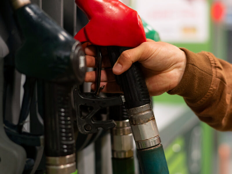 Close-up of a person selecting a red fuel nozzle at a gas station pump