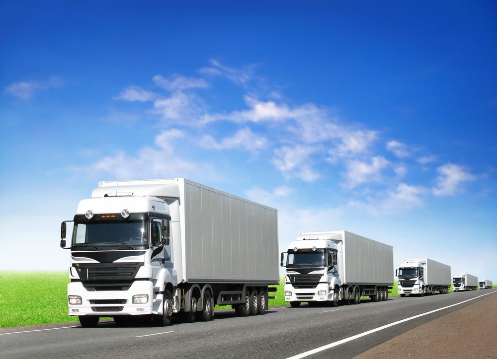 Caravan of white trucks on country highway under blue sky