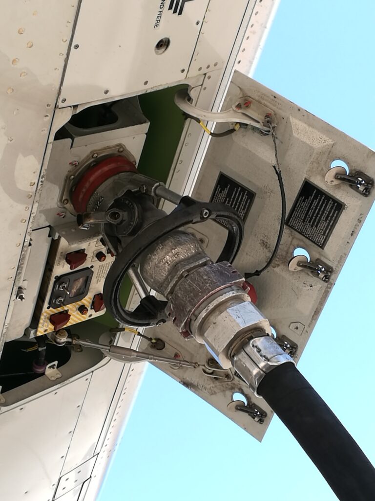 Close-up of Jet-A fuel hose connected to aircraft fueling port, showing aviation fueling operation.