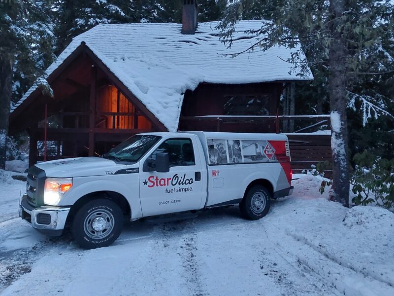 Star Oilco diesel service truck parked in front of a snow-covered log cabin in the Oregon woods
