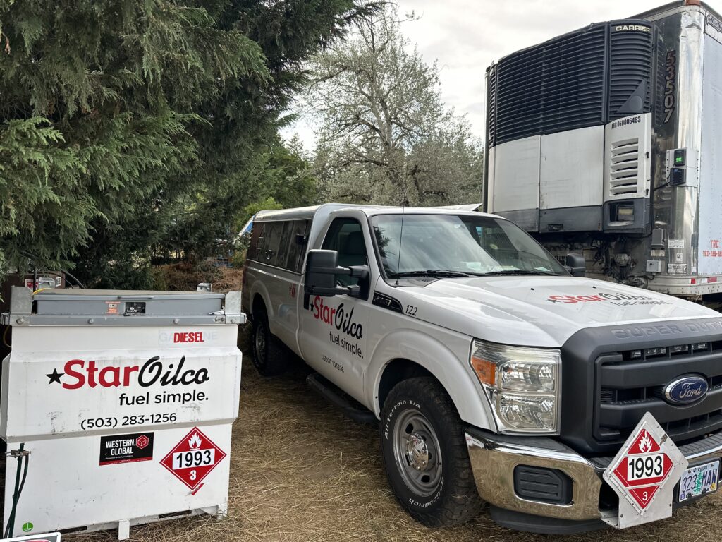 Star Oilco diesel delivery truck with portable fuel tank servicing a refrigerated trailer in a wooded outdoor setting