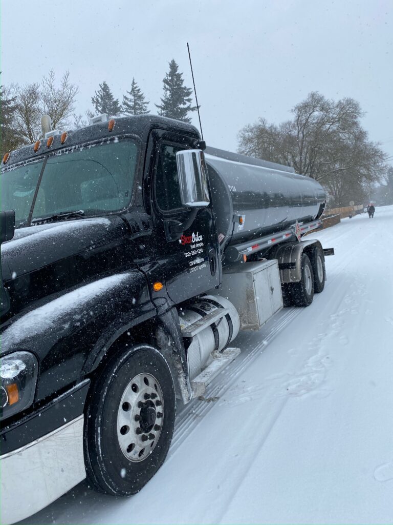 Star Oilco black fuel delivery truck driving through snow during winter storm
