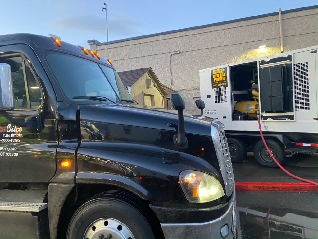 Star Oilco black fuel truck refueling a CAT rental generator at a commercial site
