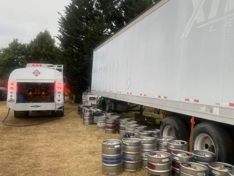 Star Oilco fuel truck delivering diesel to a refrigerated trailer at an outdoor event with beer kegs stacked alongside
