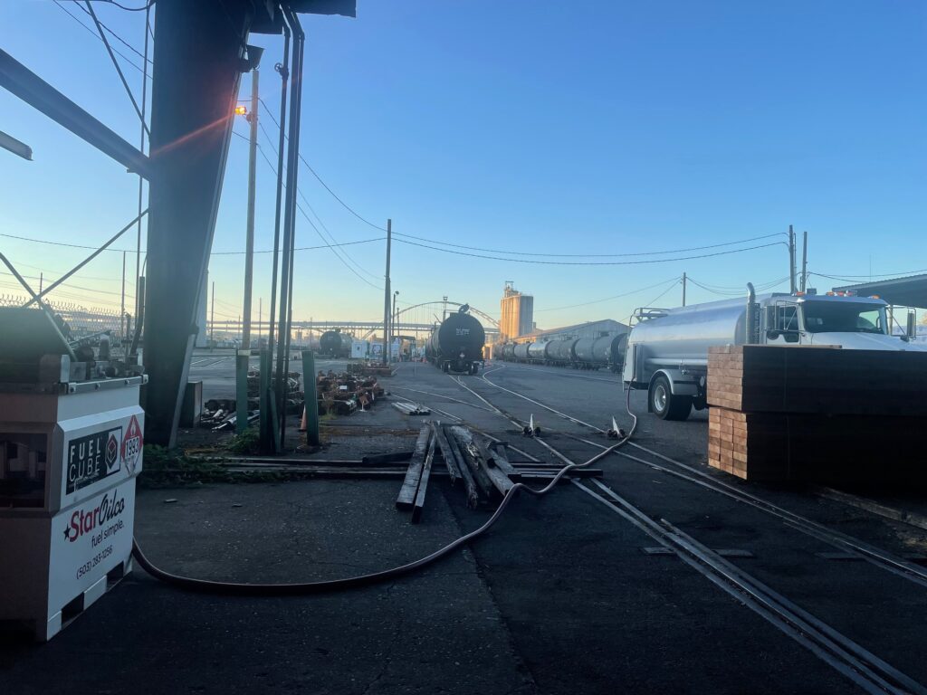 Star Oilco fuel truck delivering diesel at an industrial rail yard with rail tankers and fuel cube on site
