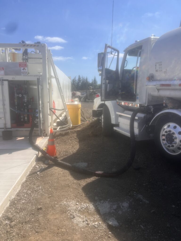 Star Oilco tanker truck fueling an aboveground fuel tank at a construction site under clear skies